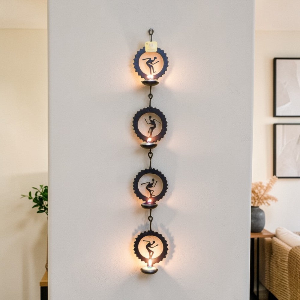 Handmade Bastar iron craft circular tea light wall hanging displayed vertically on a wall, featuring four black wrought iron circle panels with folk dancer motifs and glowing diyas
