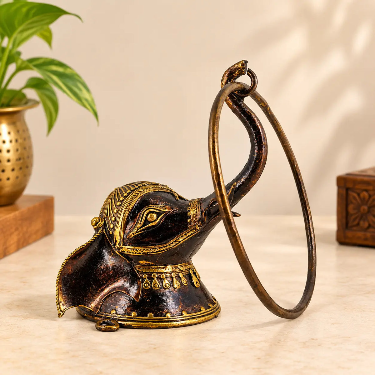 Bastar Dhokra brass elephant head towel ring with raised trunk and gold detailing, placed on a marble surface beside a brass vase