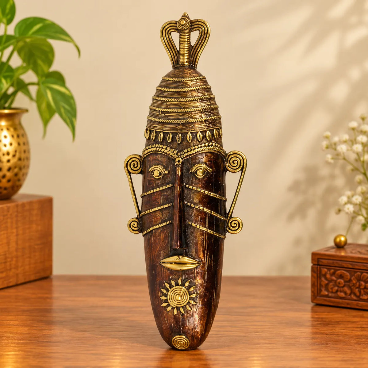 Bastar Dhokra brass long face mask with crown, spiral ears and sun motif, handcrafted decor piece on a wooden table