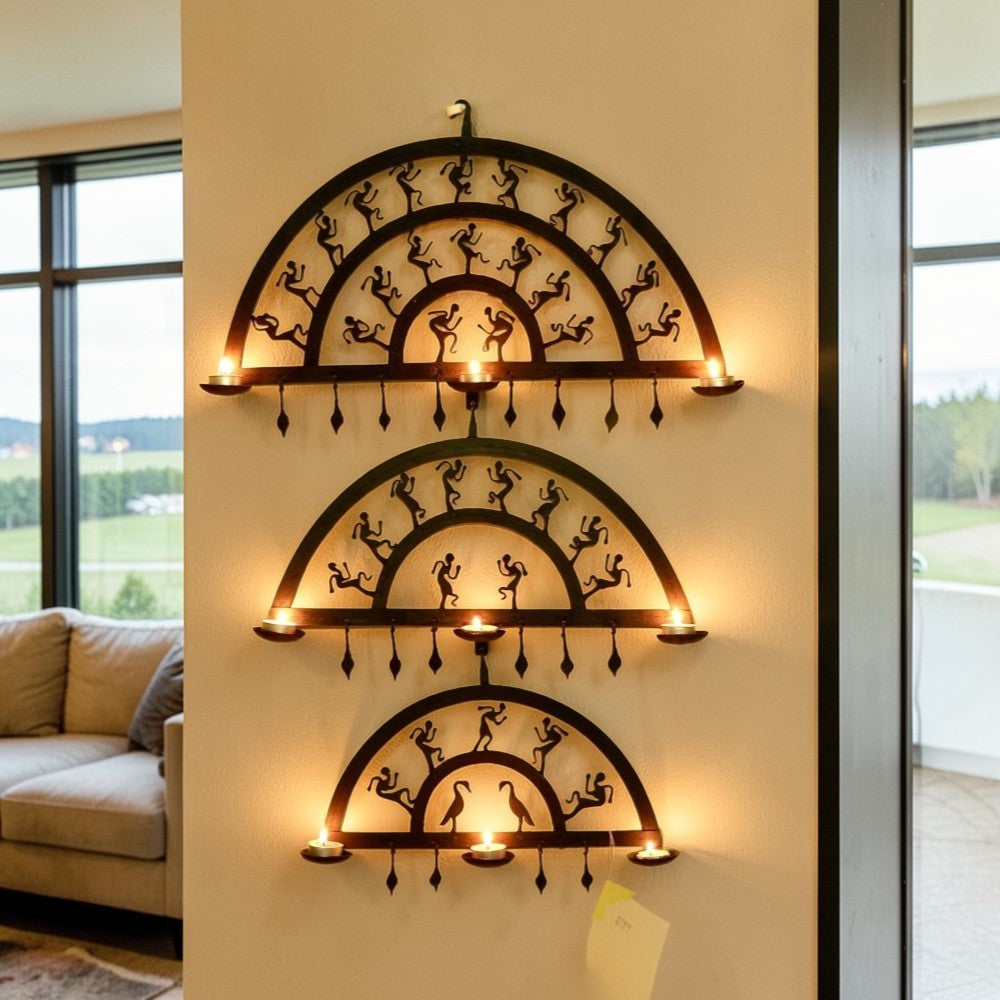 Handmade Bastar iron art half circle wall hanging displayed on a wall with lit diyas, featuring layered semicircular wrought iron frames and folk dancer motifs creating a warm ambient glow
