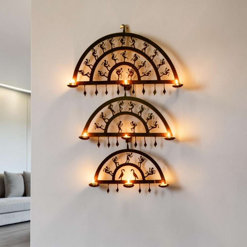 Handmade Bastar iron art half circle wall hanging displayed on a wall with lit diyas, featuring layered semicircular wrought iron frames and folk dancer motifs creating a warm ambient glow