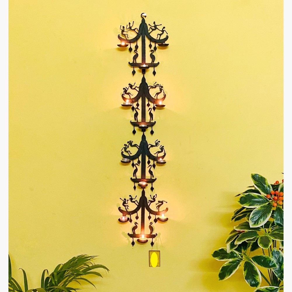 Handmade Bastar iron art moustache design tea light wall hanging displayed vertically on a wall, featuring black wrought iron structure with multiple diya holders creating a warm ambient glow
