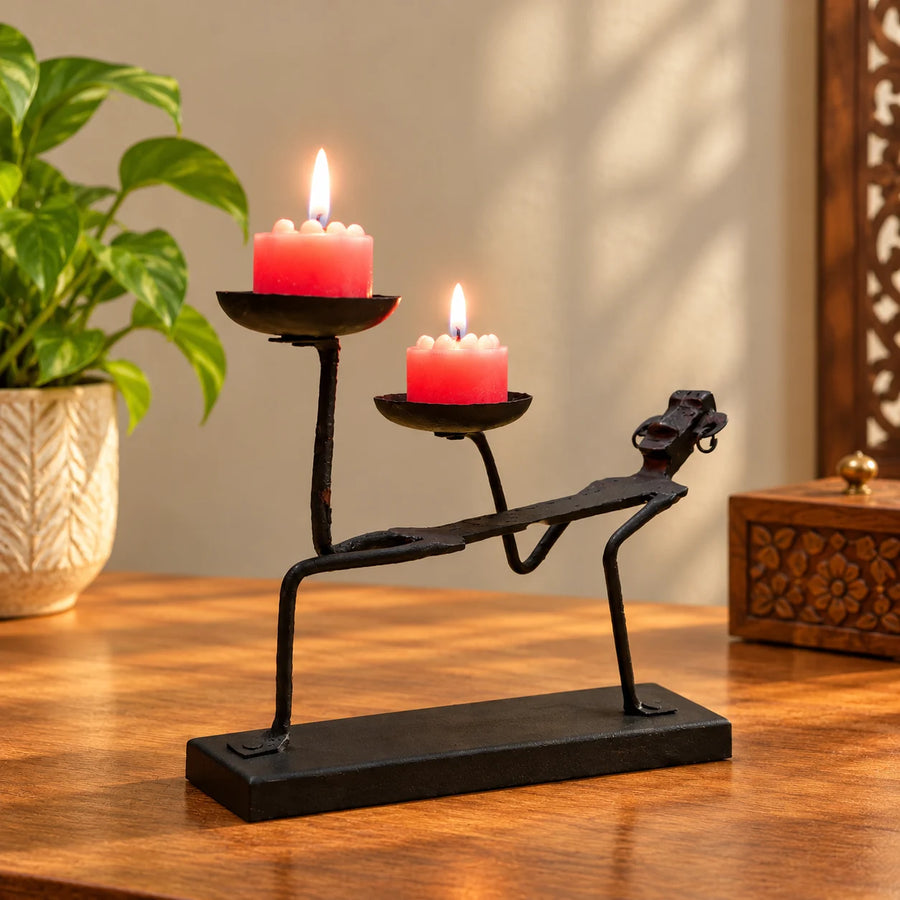 Bastar Loha Shilp wrought iron double tealight holder shaped like a figure in a stretching pose, with two lit candles on a wooden table