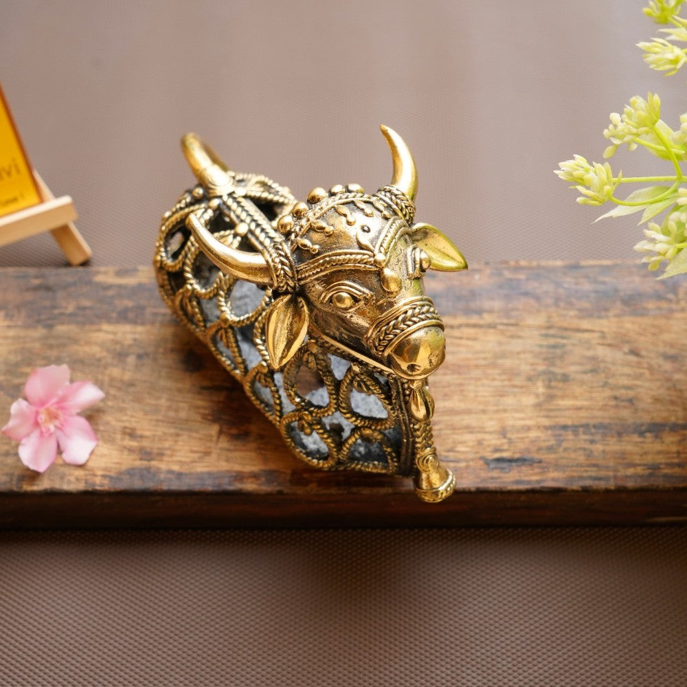 Handcrafted brass Nandi sitting statue placed as a spiritual home décor accent with lamp light enhancing jali work