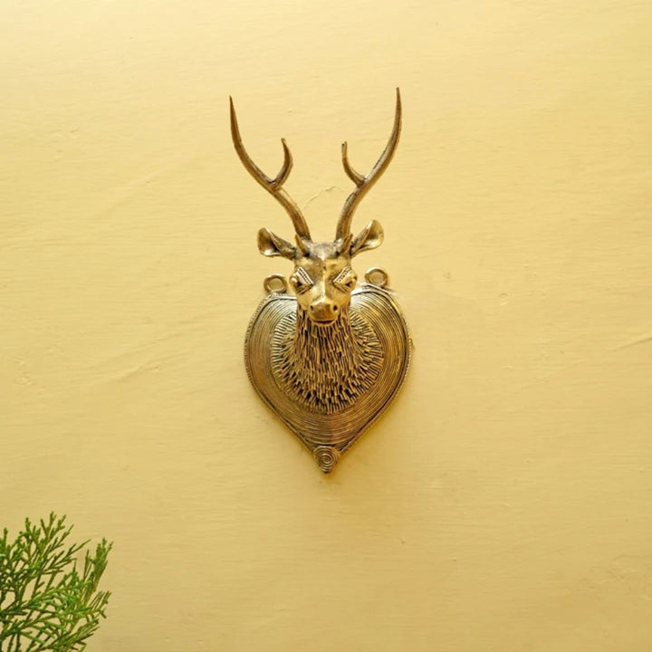 Handcrafted brass Bastar Dokra deer head wall hanging displayed on a warm textured wall, showcasing traditional metal craftsmanship
