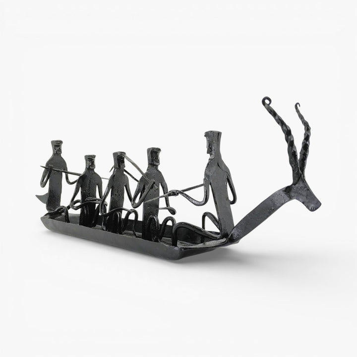 Front angled view of handcrafted Bastar iron art Kerala boat tabletop showpiece featuring tribal figures and rustic black finish
