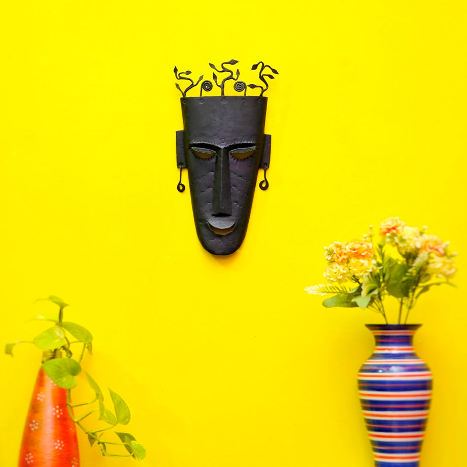 Handmade Bastar iron tribal wall mask with abstract tree crown, black matte finish, displayed on colorful living room wall decor