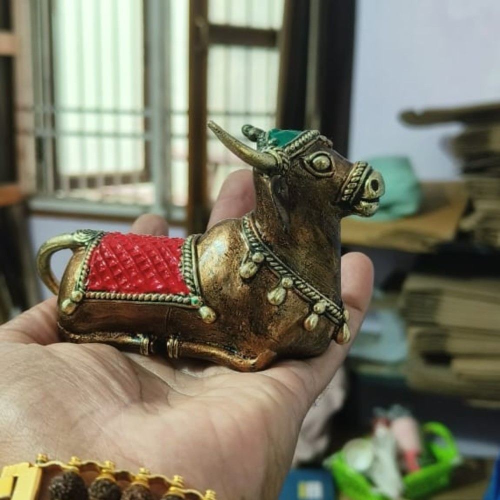 Handheld view of Sacred Calm Nandi figurine in Bastar Dokra art, handcrafted brass sculpture with red detailing