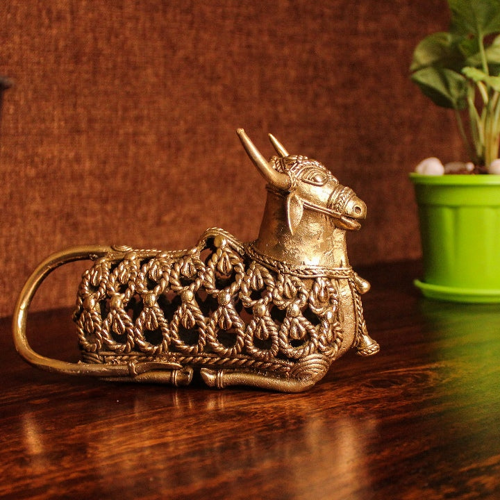 Handcrafted brass Nandi sitting statue with intricate jali work displayed on a wooden surface in warm indoor lighting